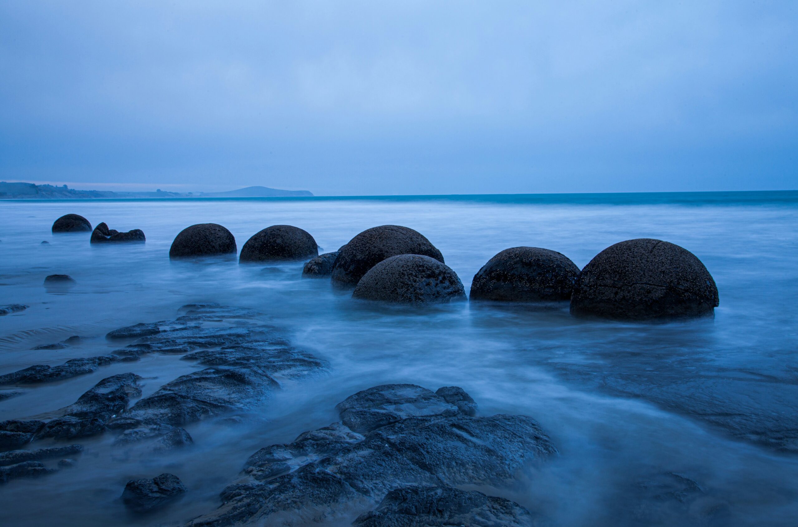 moeraki boulders visible in a dusky blue light with sea washing over them